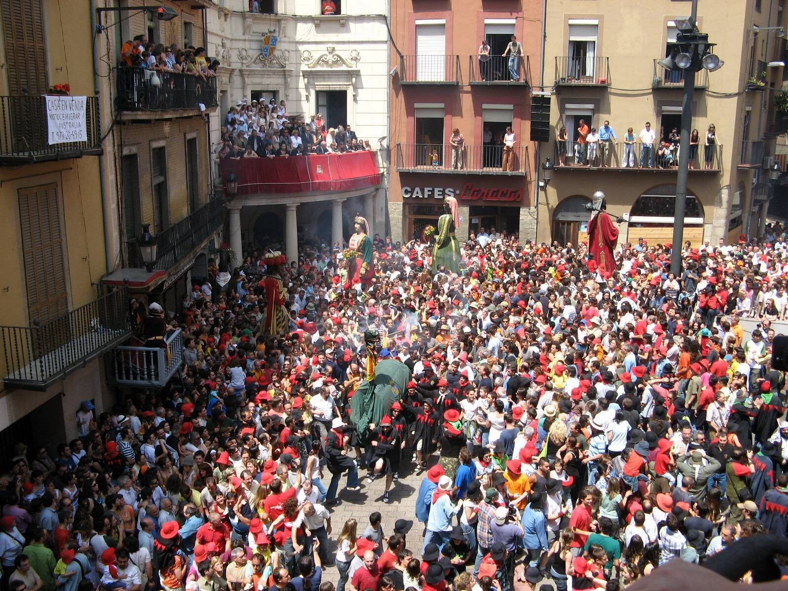 La plaça de Sant Pere de Berga abarrotada durante una passada de la Patum, con los gegants y una guita abriéndose paso entre la multitud vestida de rojo