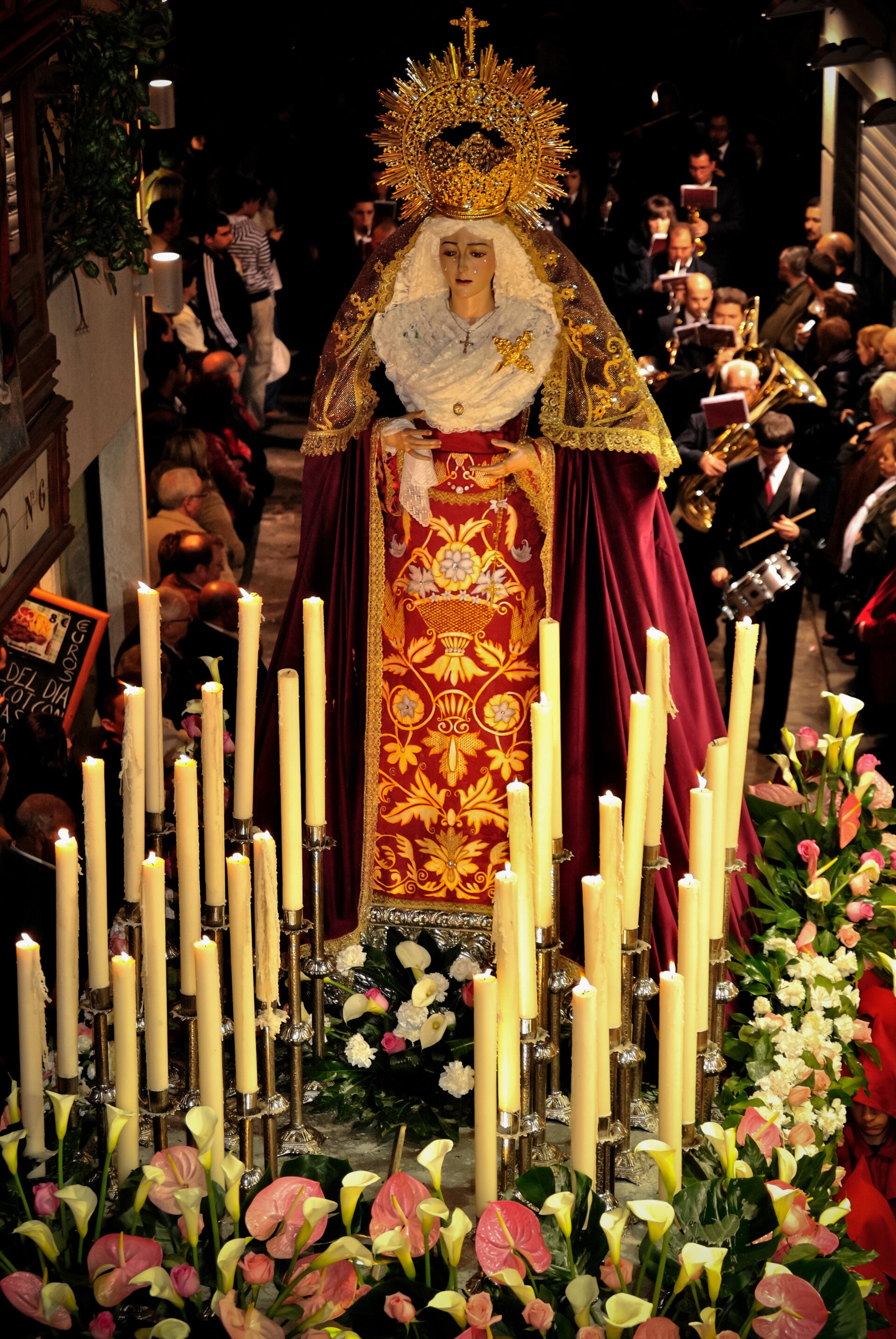 Paso de la Virgen de la Caridad entre velas y flores, de noche por una calle de Toledo, el Viernes Santo