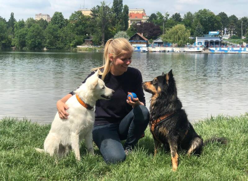 Nicole - Hundetrainerin in Baden, sitzt vor einem Fluss in der Wiese mit ihren beiden Hunden Barney und Tarzan