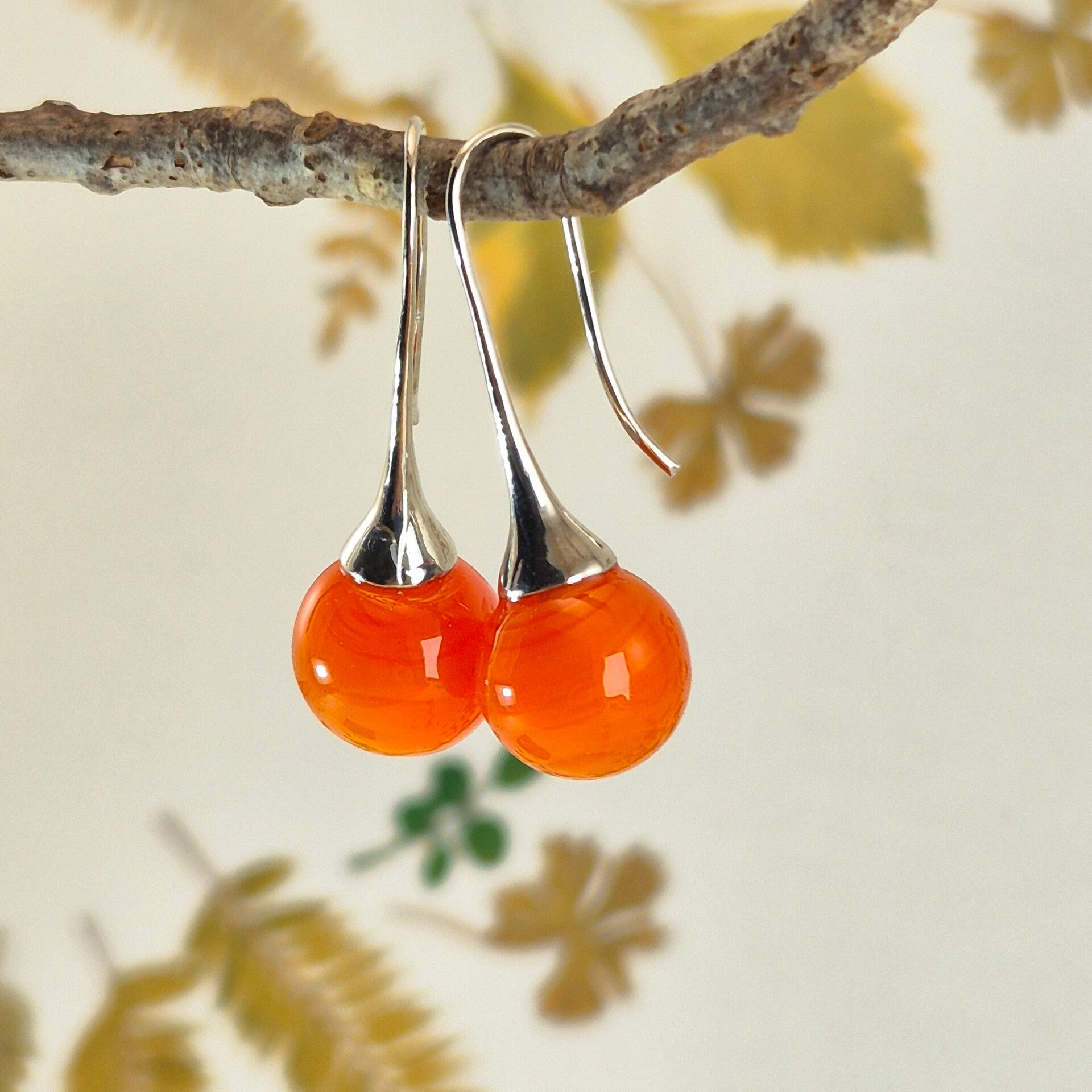 Trompet oorbellen met bolletjes van semi-transparant oranje glas met iets streeppatroon