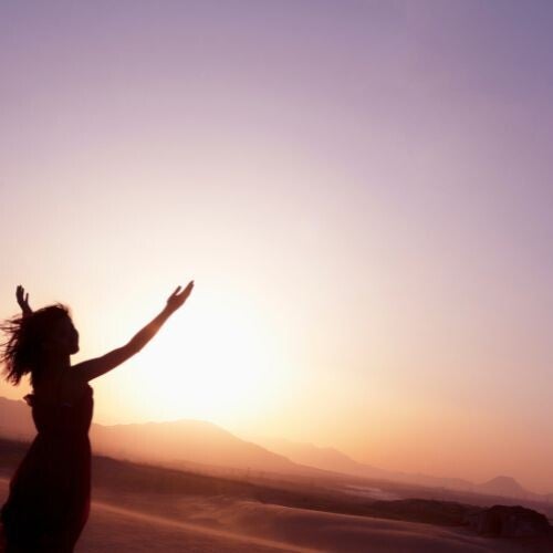 Femme qui lève les bras face à la montagne, avec des couleurs douces, inspirant l'énergie et la paix intérieure