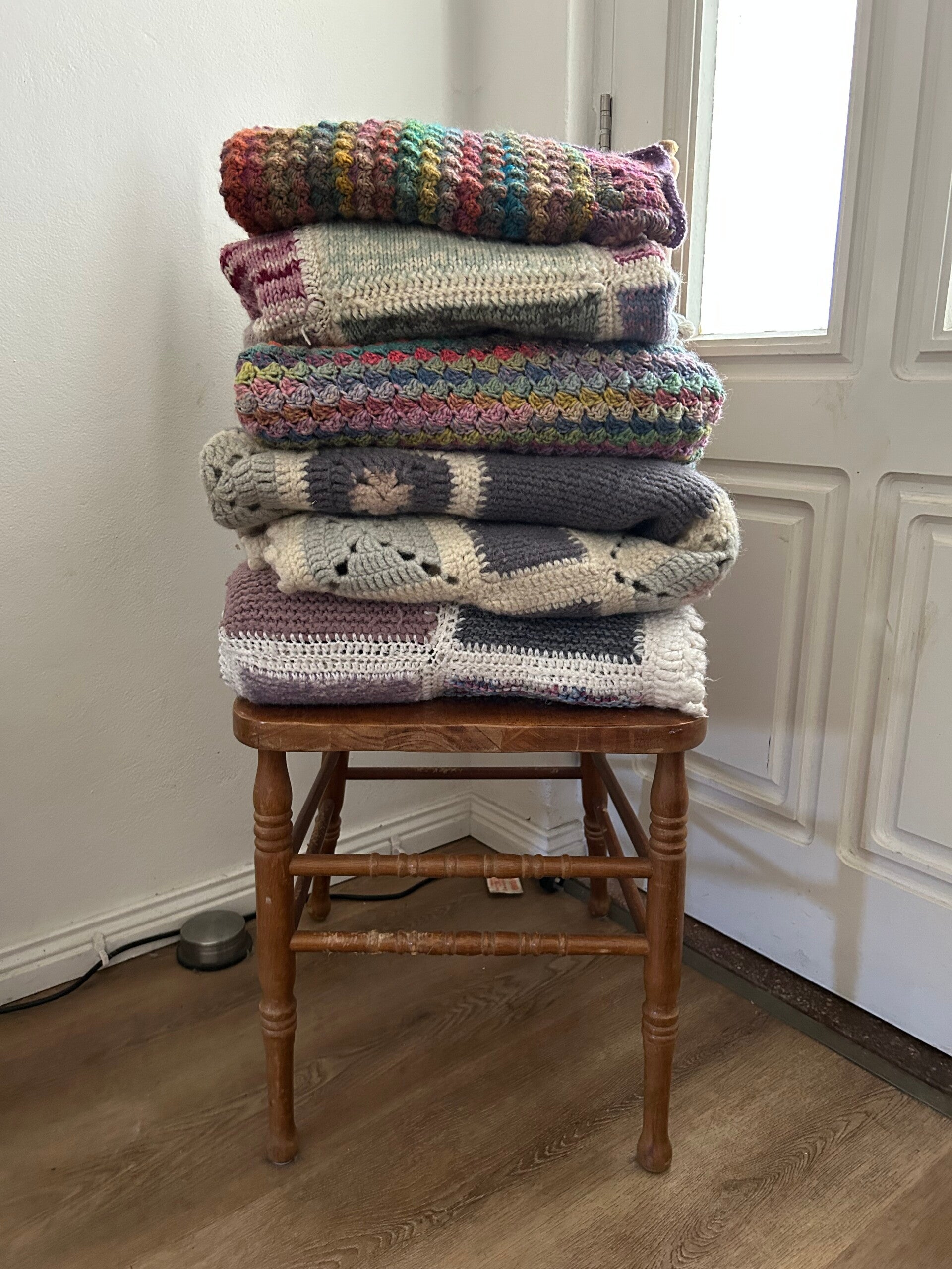2 fluffy dogs sitting on a timber floor with a rug. The dogs are wearing doggy accessories. Crocheted colourful bows on a collar around their necks.
