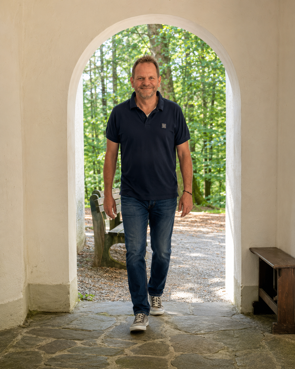 Sebastian Fehmer geht durch einen Torbogen vor einem Wald.