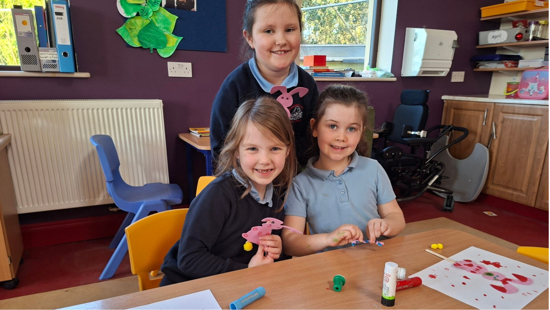 Three smiling girls show thier projects in art class.