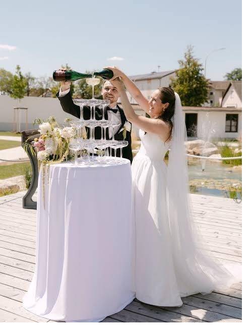 Brautpaar gießt gemeinsam Champagner auf eine Sektpyramide bei einer Hochzeit im Freien.