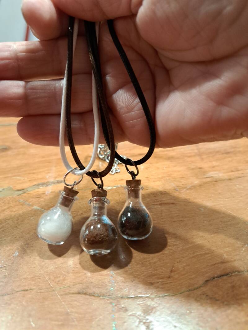 Drie koordkettingen met glazen flesje als hanger in verschillende tinten alpacawol