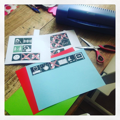 Foto van uitgeprinte pictogrammen, papier, schaar en een lamineerapparaat om zelf pictogrammen te maken voor mijn kinderen met autisme.