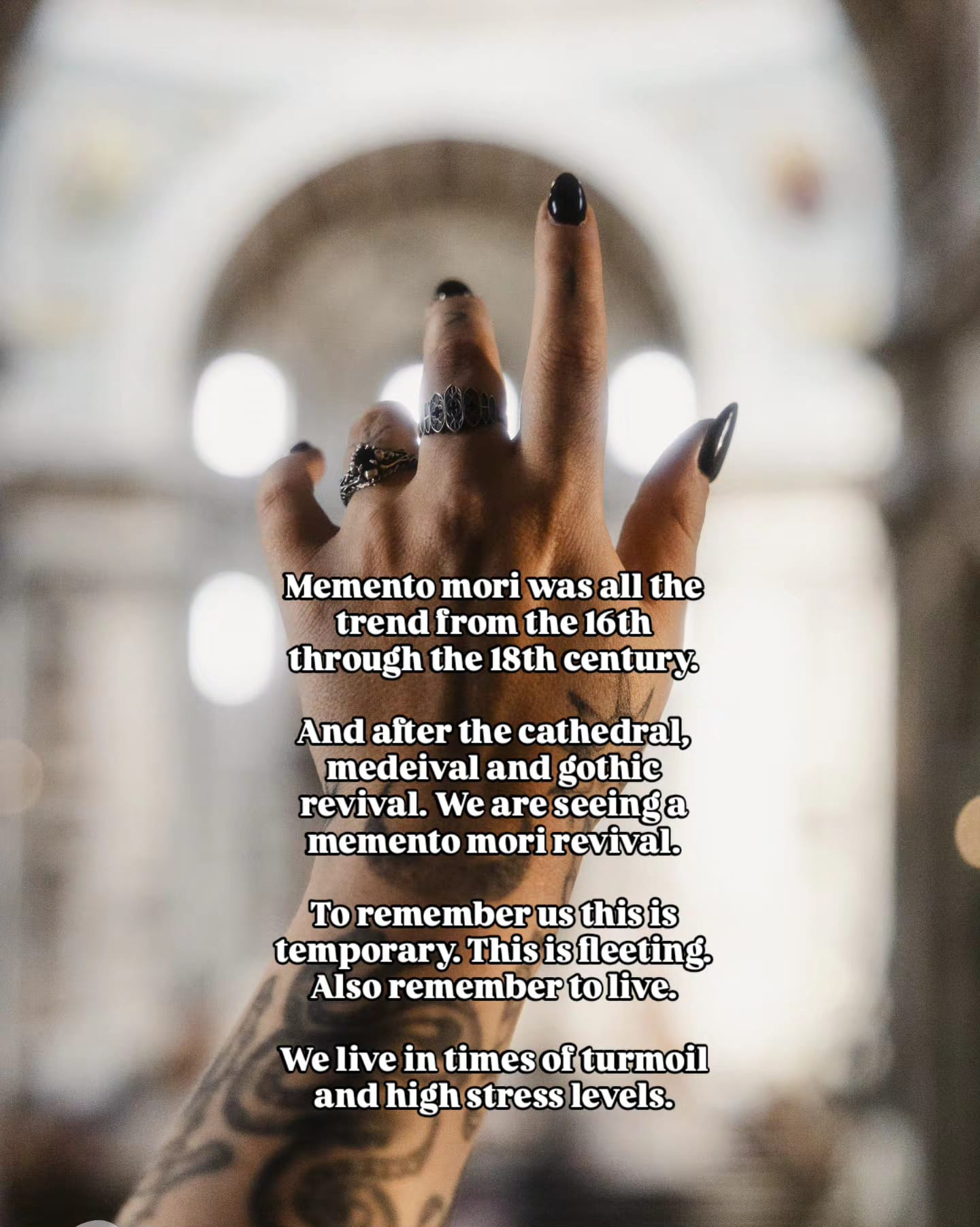 Tattooed hand raised inside a cathedral wearing handmade gothic silver memento mori rings