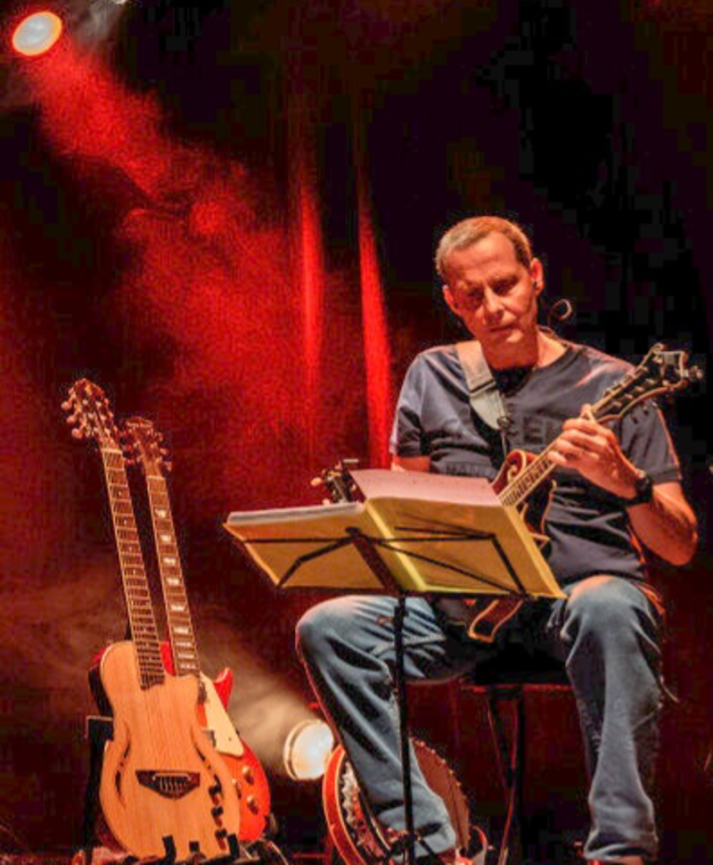 Tony Ros à la mandoline, entouré de ses guitares.