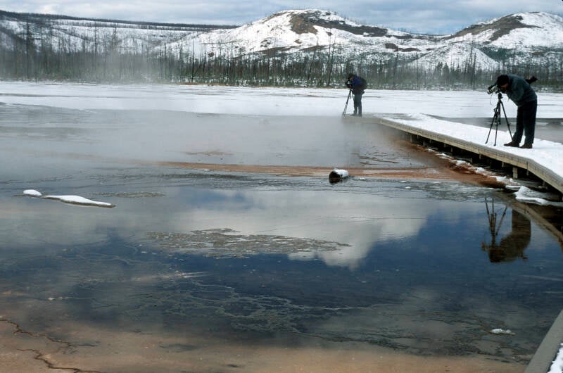 Photographers photographing Yellowstone National Park lake with ice and snow background mountains walkway and reflecions