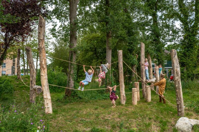 kinderen spelen in de natuurspeeltuin, een moeder kijkt toe
