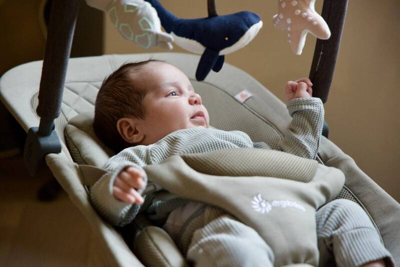 Baby in wipstoeltje kijkt naar mobiel met knuffels tijdens newbornshoot Den Haag