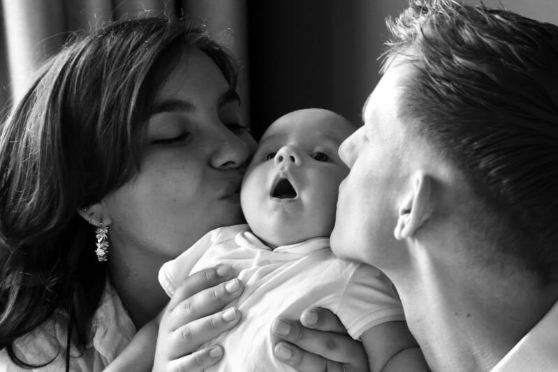 Portret van pasgeboren baby die kus krijgt van vander en moeder.  Dichtbij gefotografeerd, sfeerbeeld bij blog over newbornfotograaf Den Haag