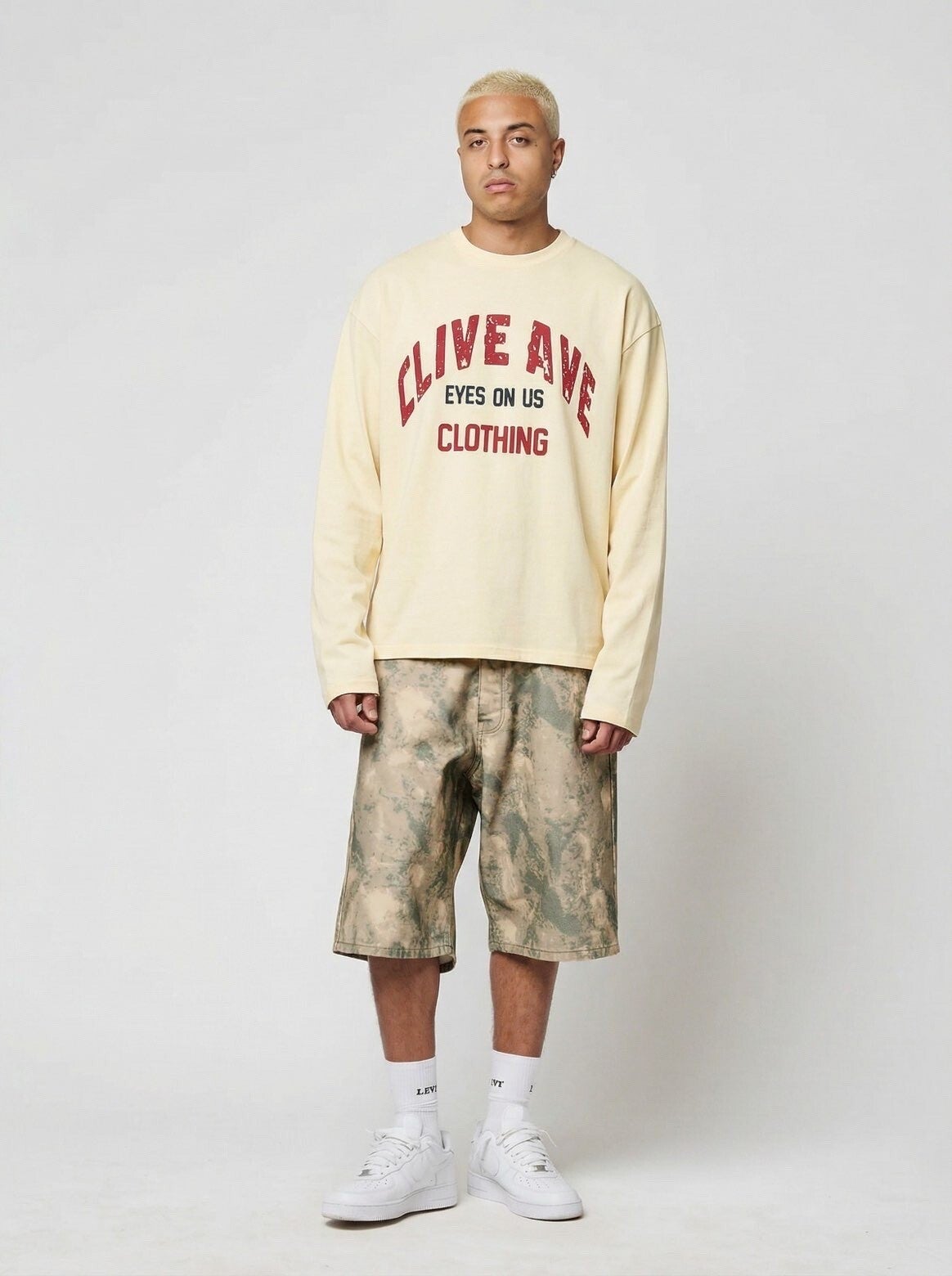 Voorkant van de off-white boxy fit streetwear longsleeve van Clive Ave. Voorzien van rode vintage 'Clive Ave Clothing' en zwarte 'Eyes On Us' bedrukking, gedragen door een model.