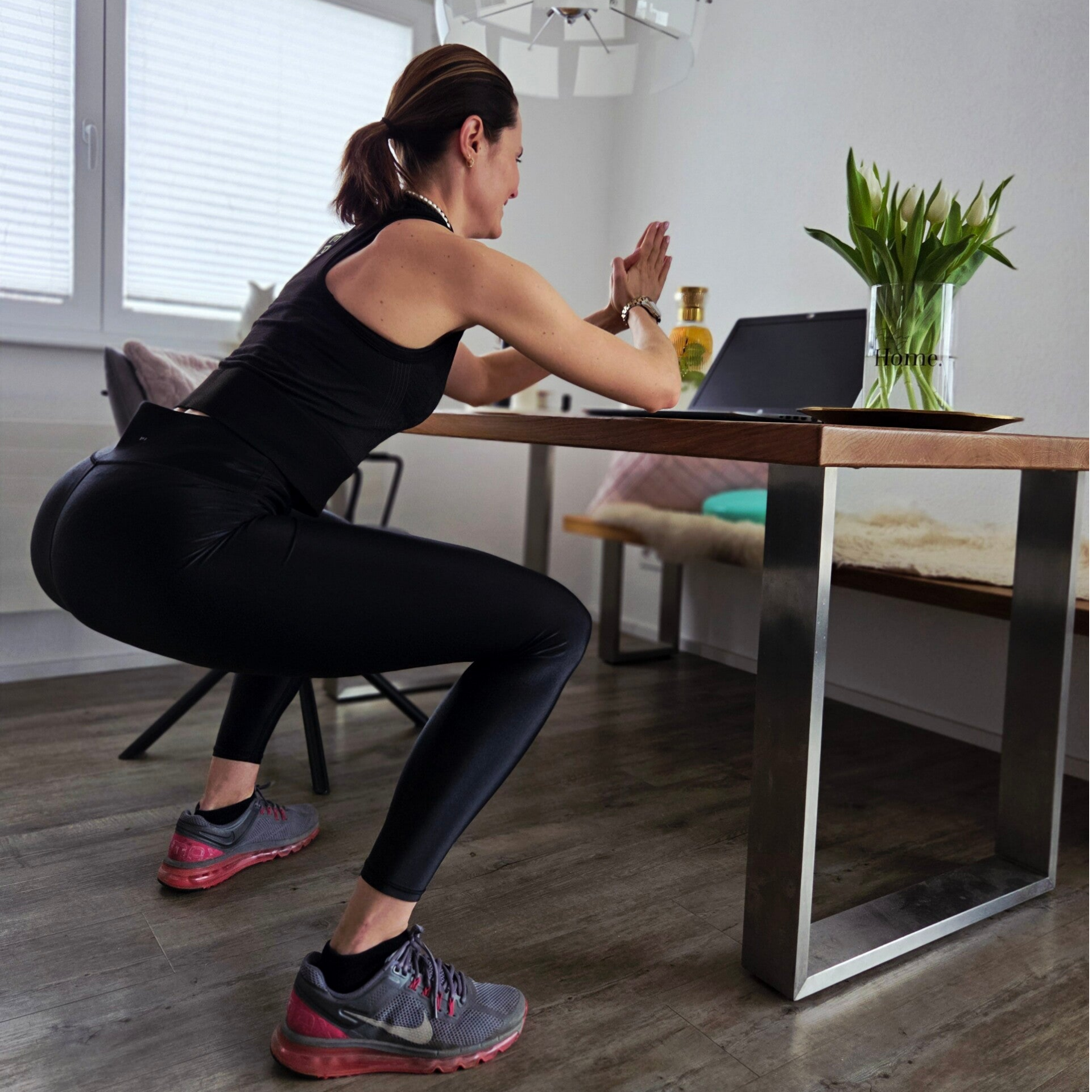 Die Trainierende steht an einem Tisch mit einem Laptop vor sich und bekommt Anweisungen online von der Personal Trainerin.