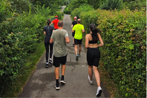 Die Mitarbeitenden joggen durch eine Kleingartenanlage und haben Freude dabei.