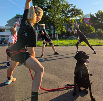 Die Trainerin macht zum Trainingsabschluss ausgiebige Dehnübungen mit den Mitarbeitenden. Auch ihr Hund ist mit dabei.