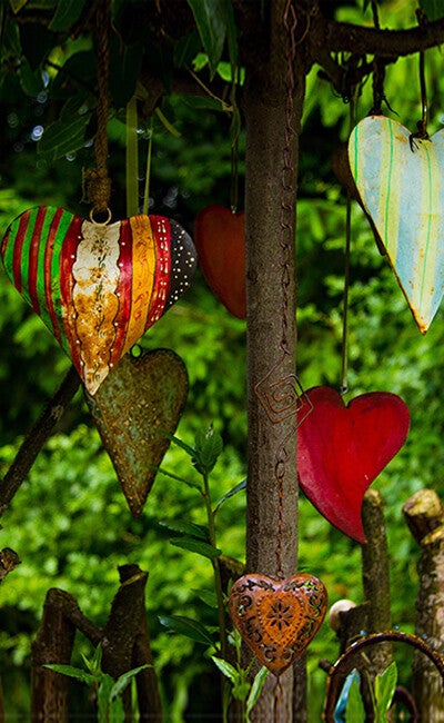 Gekleurde houten harten hangen aan touwtjes in een groene natuurlijke omgeving als symbool voor verbinding, liefde en groei.