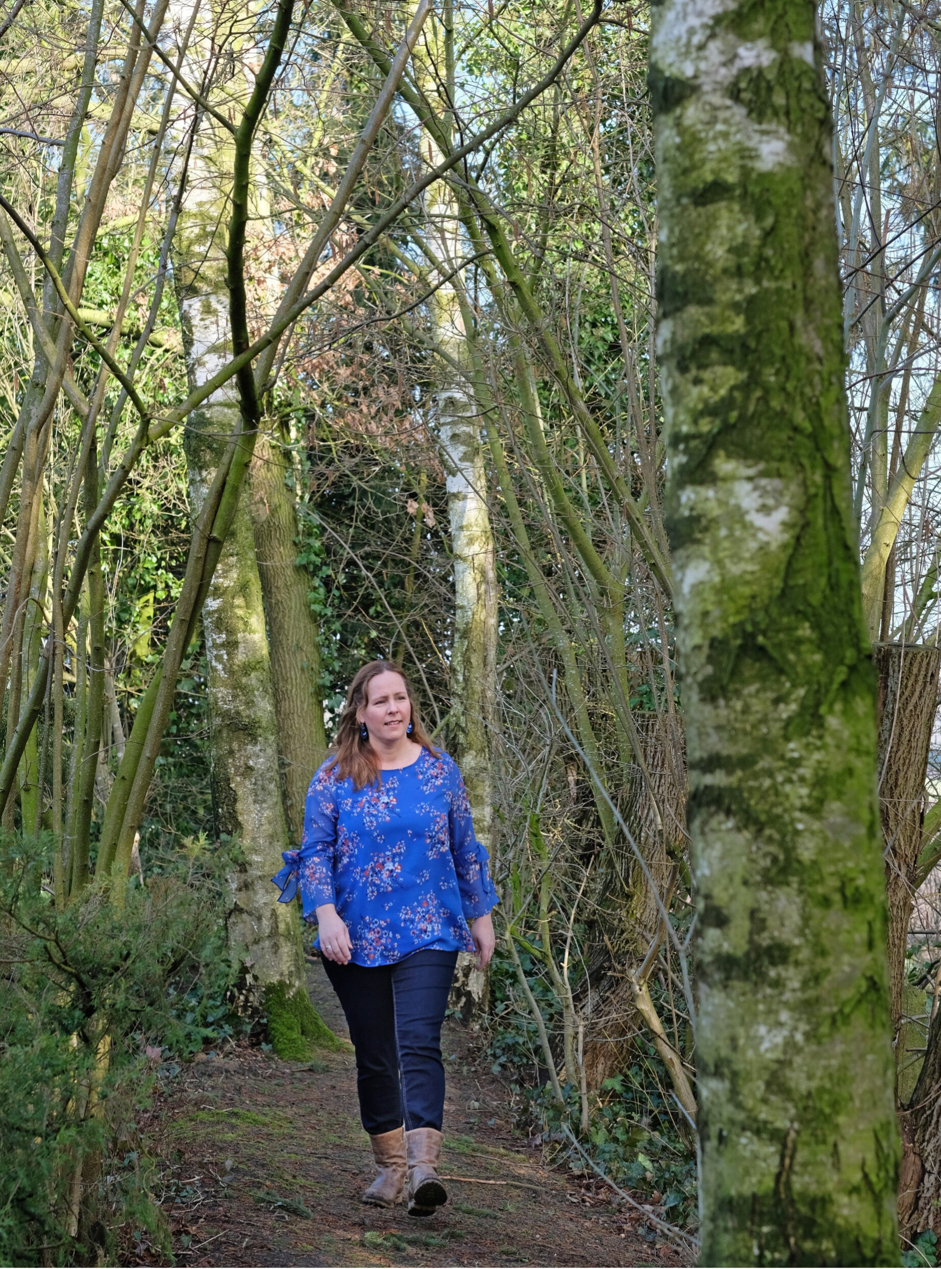 Vrouw wandelt rustig over een bospad tussen groene bomen, symbool voor persoonlijke groei, rust en balans — psychosociale therapie voor volwassen geadopteerden.