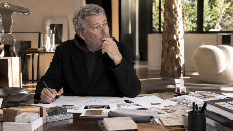 Philippe Starck travaillant sur des plans et des échantillons de matériaux dans un intérieur contemporain
