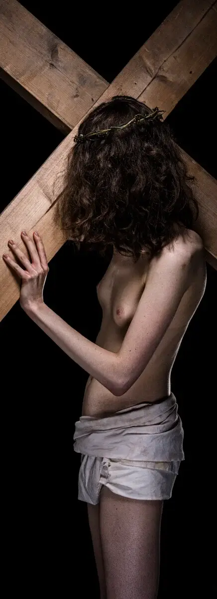 Naakte witte vrouw, profiel, draagt zwaar houten kruis met doornenkroon. Visuele tegenhanger van Imperishable, toont vrouwelijk lijden.