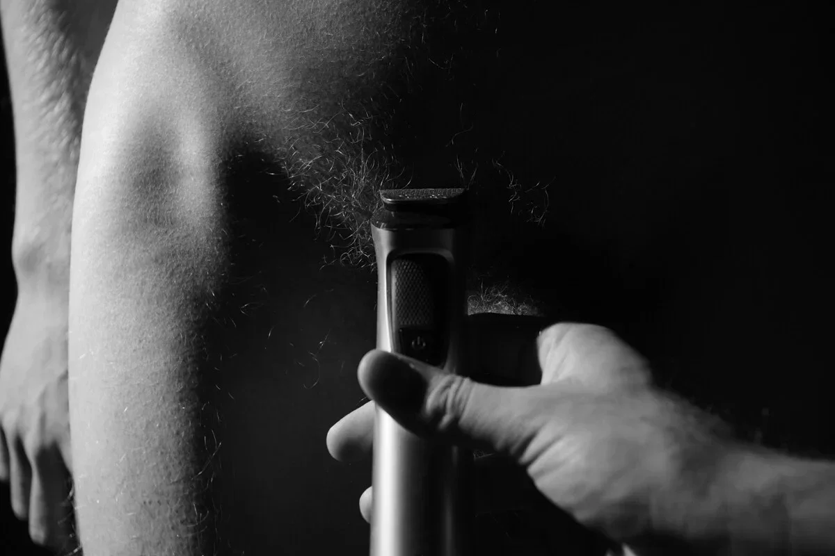 wart-wit fine art fotografie 'Grooming Ritual' van Arjan Spannenburg (2026). Intieme close-up van een mannelijk lichaam en een trimmer, waarbij de focus ligt op de tactiele textuur van de huid en het spanningsveld tussen erotiek en abstractie.