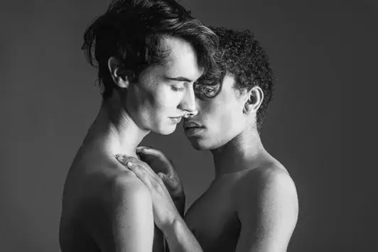 Kunstwerk PROPENSITY : Intiem portret van twee jonge mannen, voorhoofden tegen elkaar, blote schouders, zacht strijklicht, zwart-wit kunstfoto.