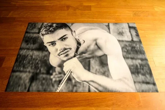 Zwart-wit tapijt op houten ondergrond toont liggende man die omhoog kijkt. Het kunstwerk als vloerobject confronteert de toeschouwer met maatschappelijke druk.