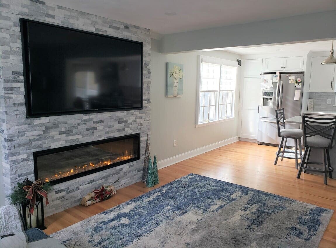 View from the family room into the renovated kitchen showing the removed wall and a stone fireplace with mounted TV.