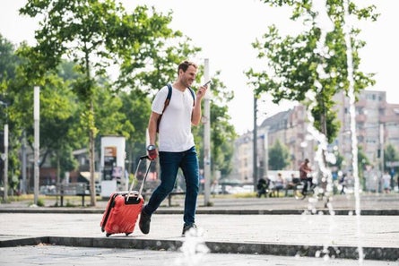 Expat carrying a suitcase, talking on the phone and similing in an european city in summer
