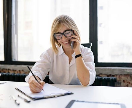 Woman smiling and talking on the phone while taking notes in an office