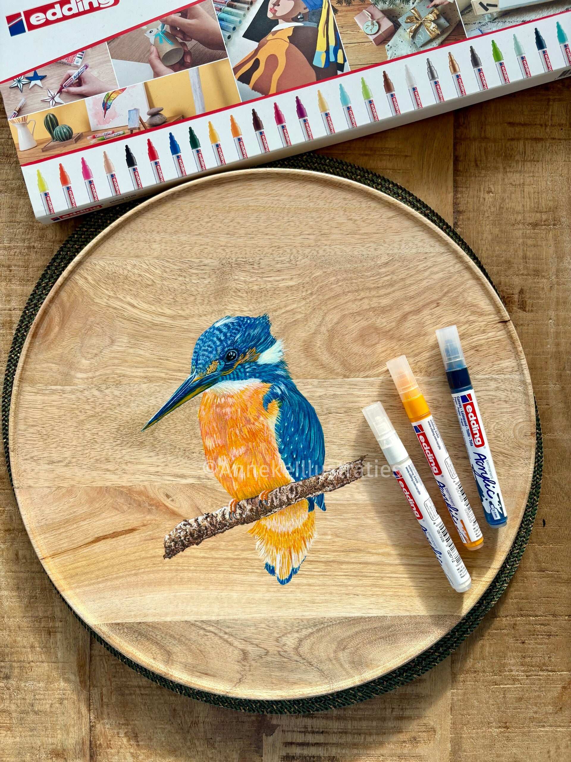 Een ijsvogel geschilderd met acrylmarkers op een rond houten bord.