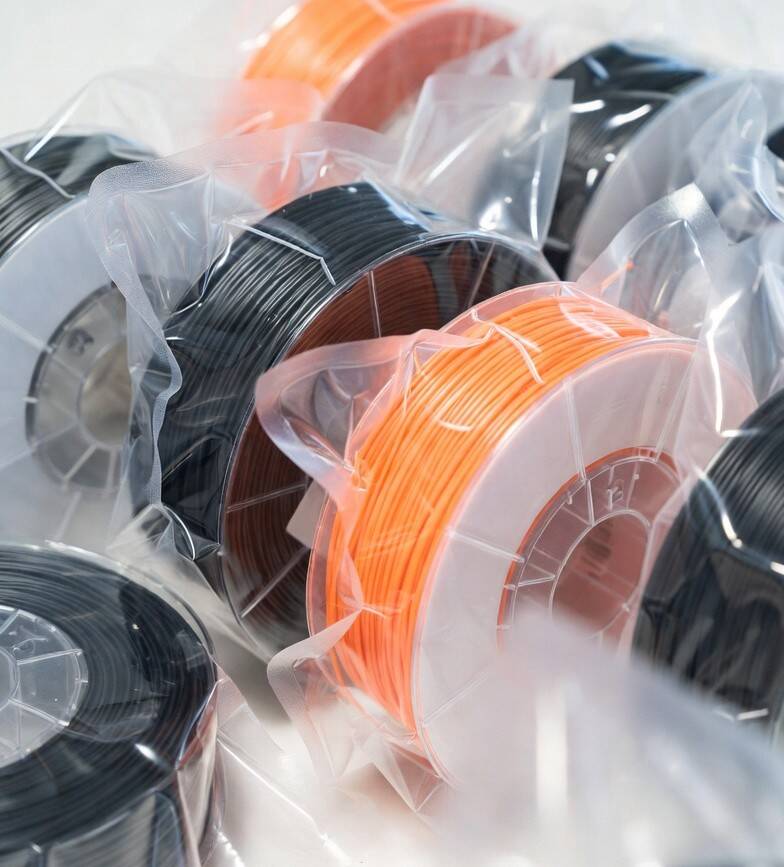 Vacuum sealed black and orange 3D printing filament spools stored properly in clear bags at 3D Creations workshop in Bangor PA