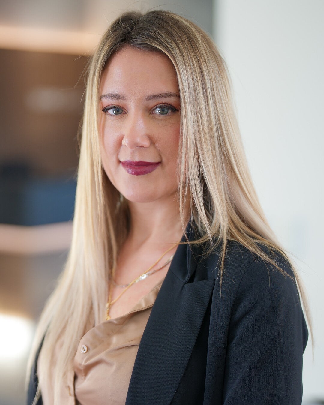 Frau sitzt auf Tischkante im modernen Büro, trägt schwarzen Blazer und beige Bluse.