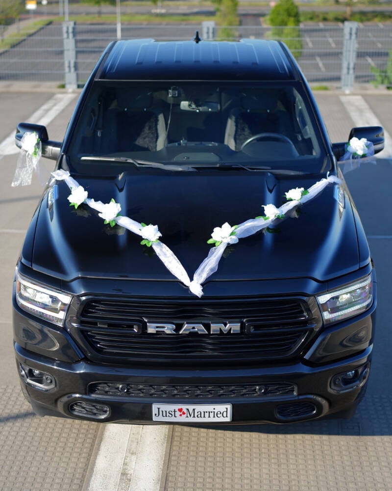 Geschmückter schwarzer RAM‑Pickup mit „Just Married“-Schild als Hochzeitsauto im Freien.