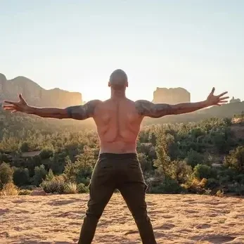 "Man standing with arms open towards sunrise in a mountain landscape, symbolizing wellness and vitality