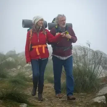 “Smiling couple hiking together on a misty mountain trail, representing vitality and connection through wellness.”