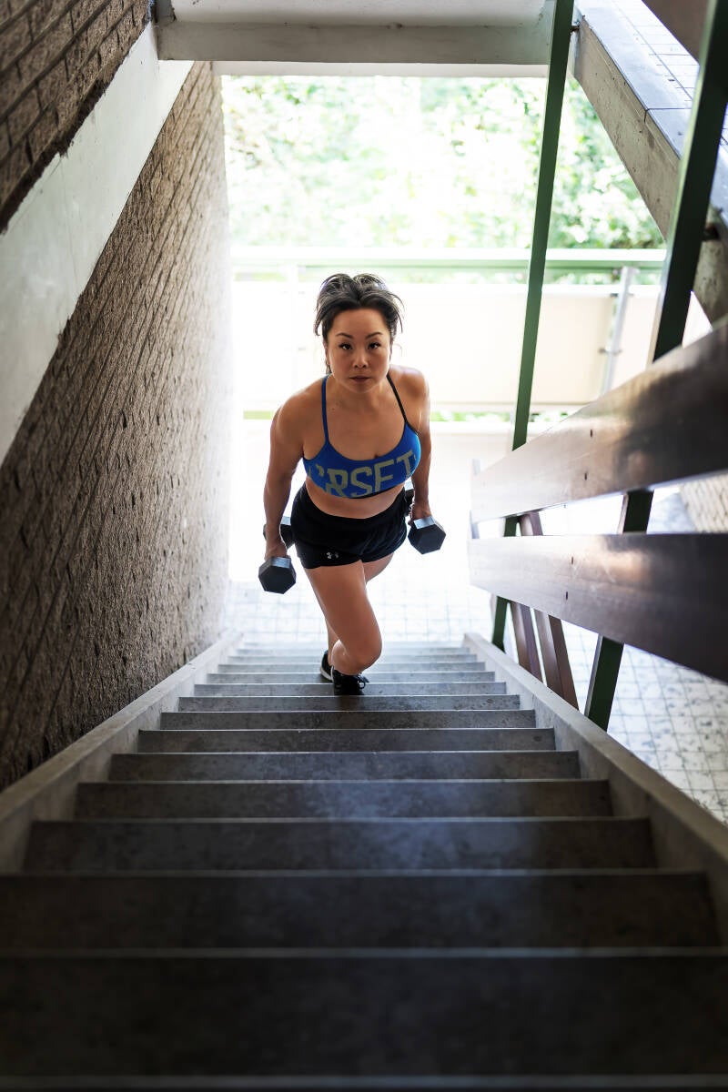 vrouw in sportkleding  staand op een trap met dumbells in haar handen