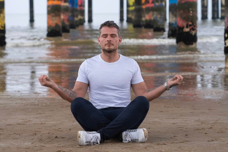 man zittend op het strand van scheveningen onder de pier in lotus houding