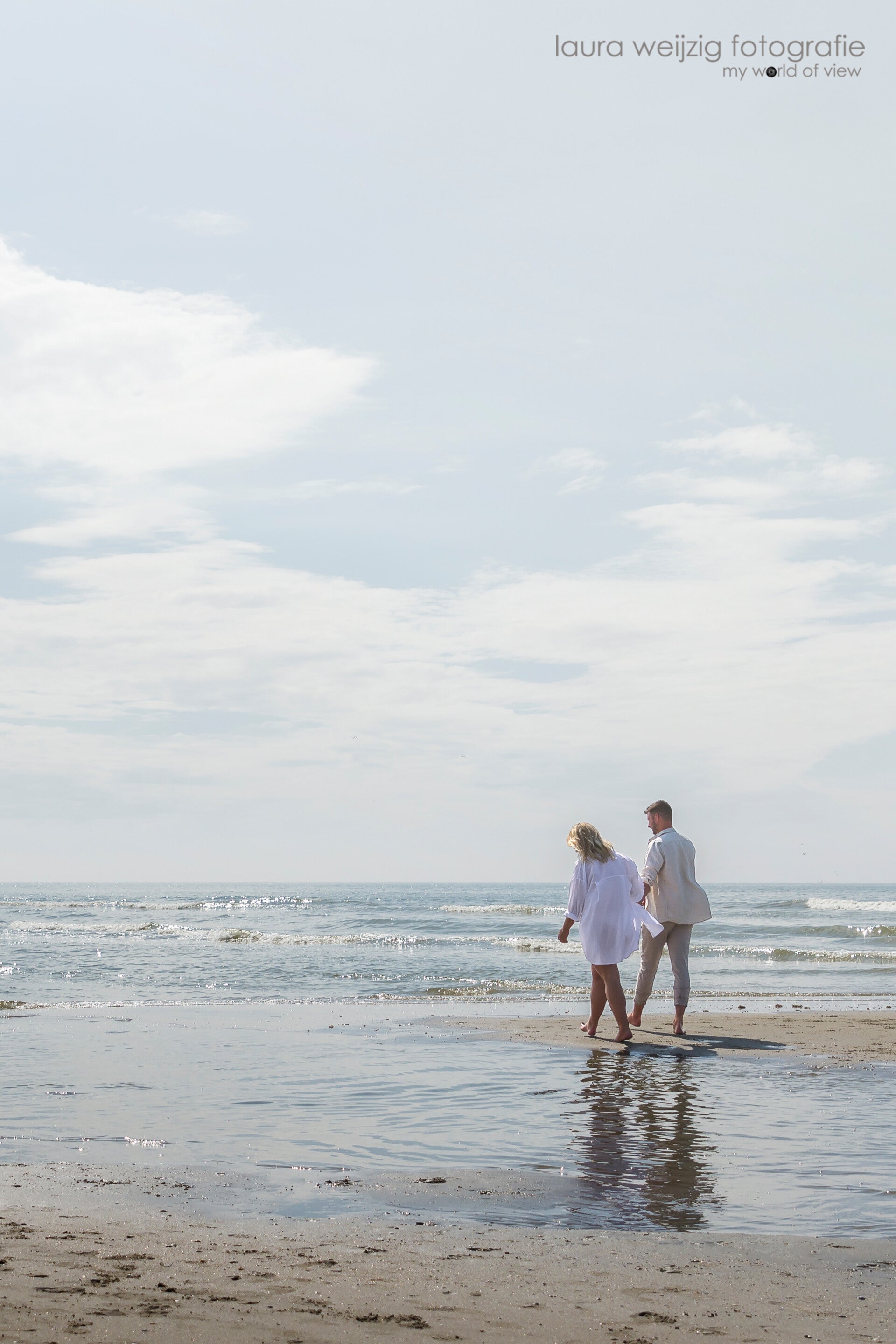 koppel paar lopend op het strand en de zee met wit overhemd en grijze broek 