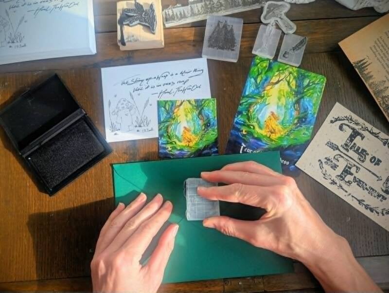 Tales of The Ever-Awt Mail Club being opened on a wooden table. A vintage letter containing a Tale, illustrations, and vintage paper goods being unveiled and read.