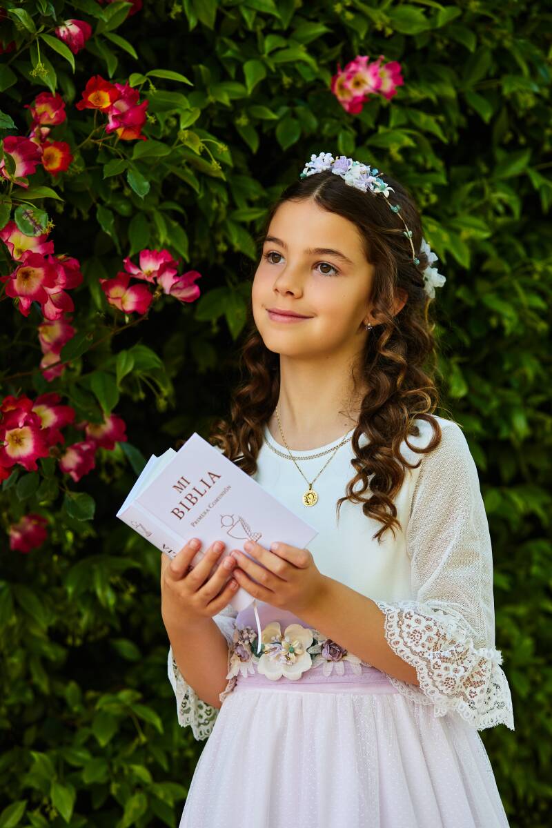 reportaje-fotos-comunion-con-biblia-madrid.jpg (Niña con Biblia en manos, rodeada de flores rosas, expresión dulce y relajada)  Ya sea en parques de Madrid, iglesias emblemáticas o en nuestro estudio con luz profesional, hacemos de cada sesión un recuerdo