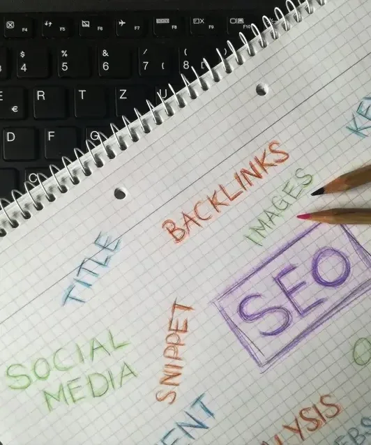 Notebook page with SEO terms like backlinks, social media and title written in colored text on a keyboard background