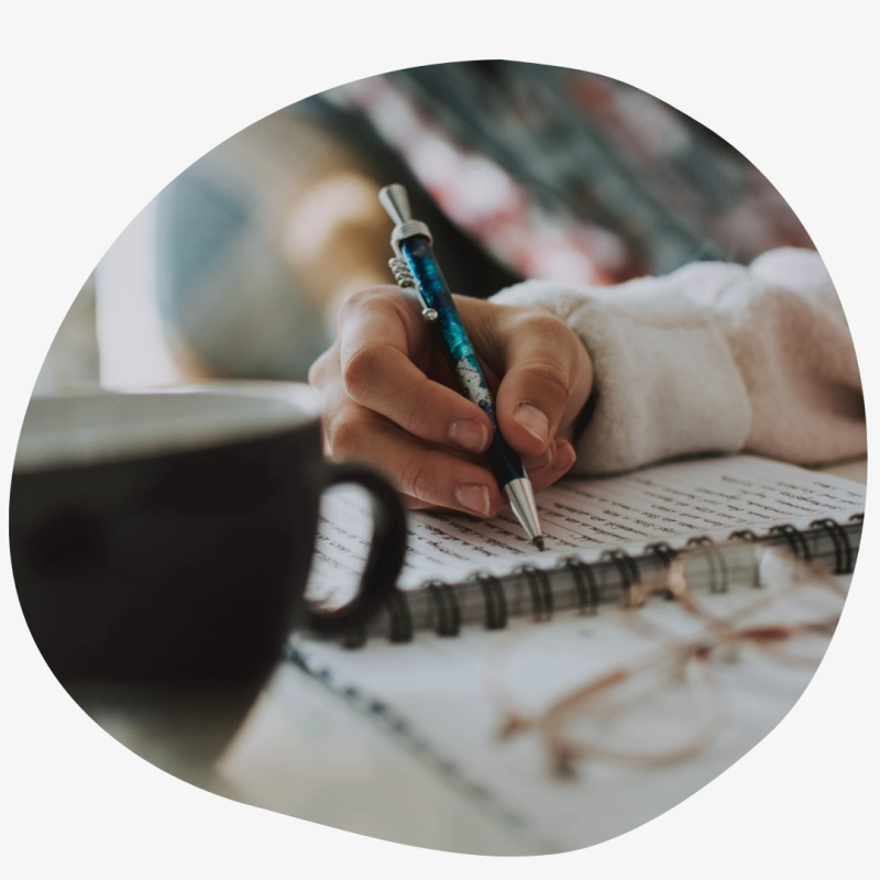 Iemand zit aan tafel en schrijft in een journal. 