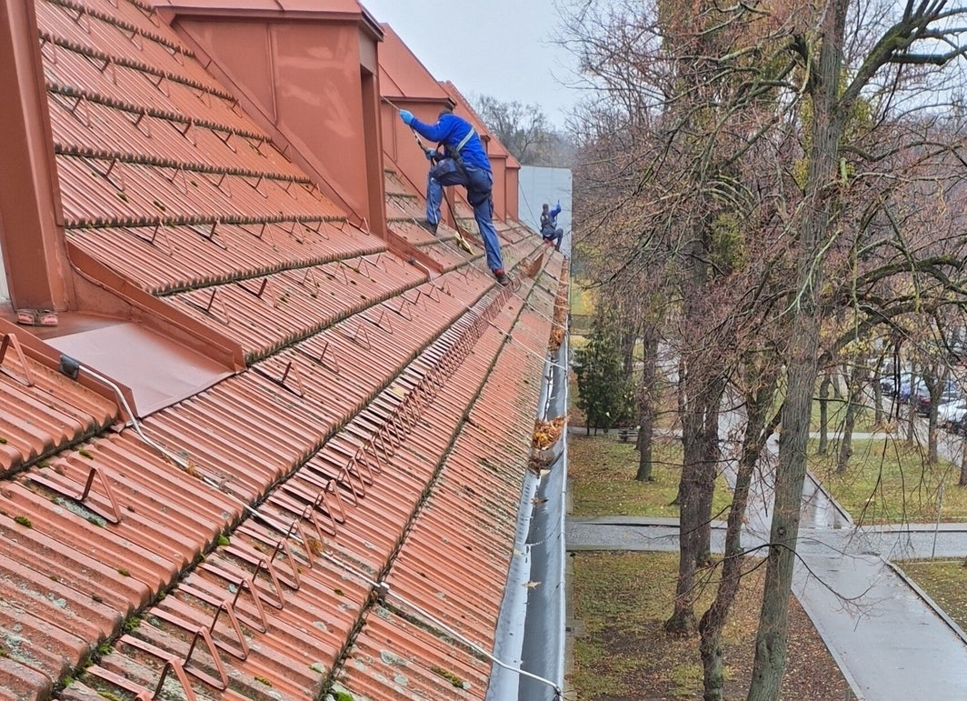 Arbeiten an der Dachrinne eines großen Gebäudes mit mehreren Dachgauben