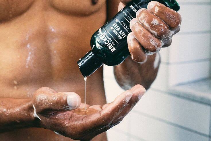 Man pouring body wash into his hand, showing off green and white product bottle as he engage in cleansing his body and stepping into his hygiene routine.