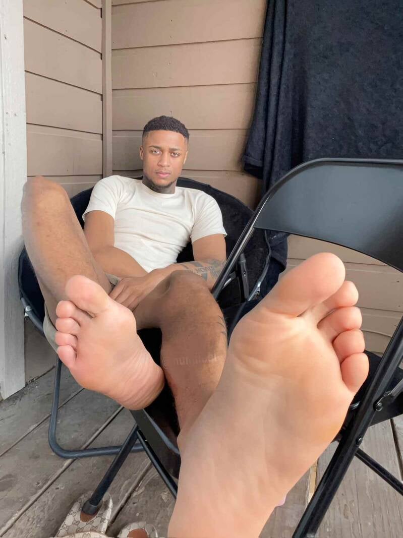 Handsome Black Man relaxing outdoors with bare feet on a chair. Allowing his big masculine feet to be seen and praised.