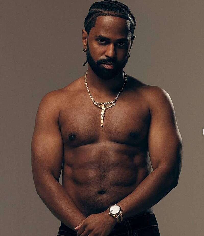 "Black man with his shirt off, standing confidently in a powerful pose, embodying strength, emotional mastery, and erotic self-control."