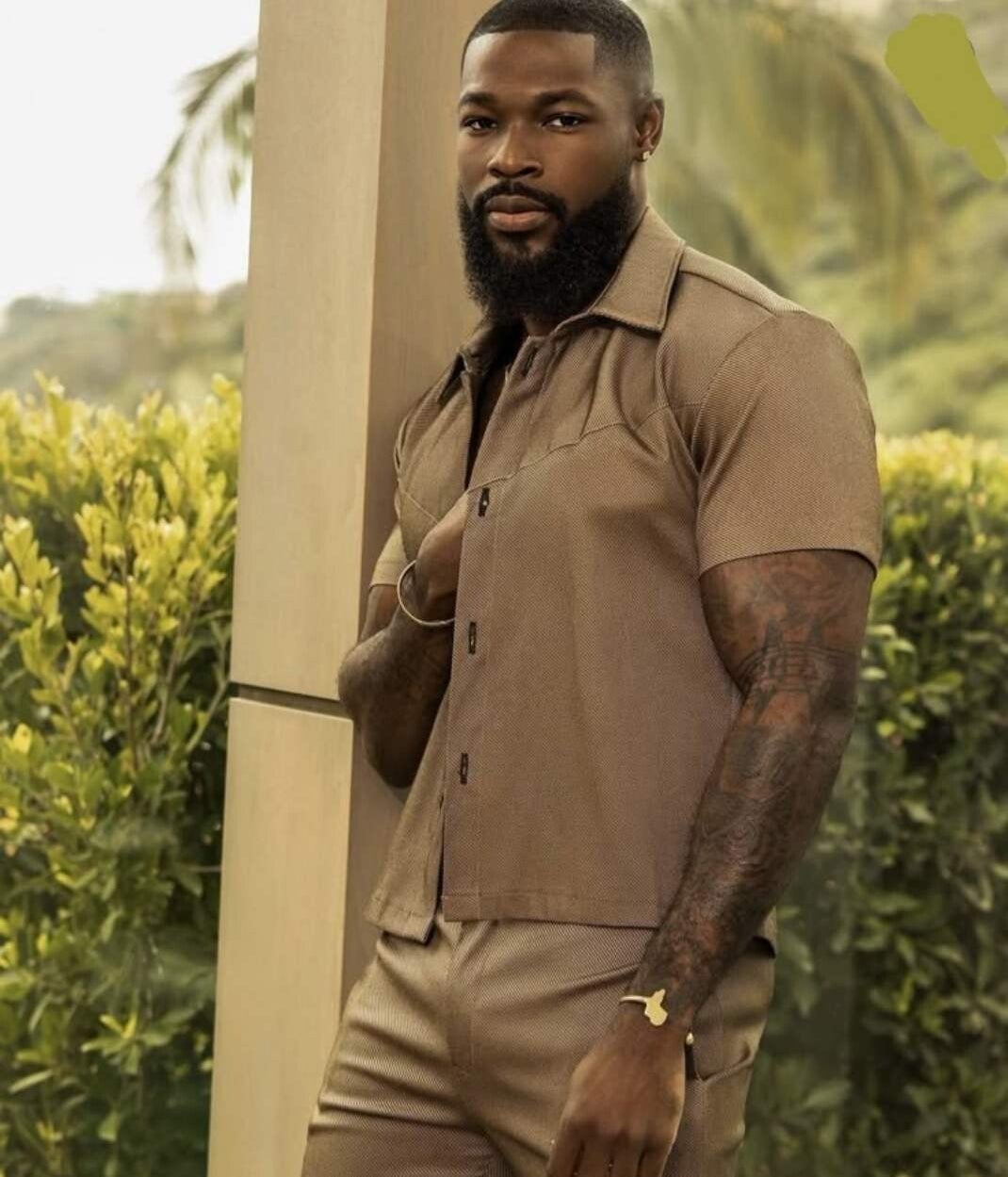 Dark-skinned Black male model wearing a brown elegant short set, confidently posing with a sexy, fashion-forward style, exuding body positivity and quiet sensuality