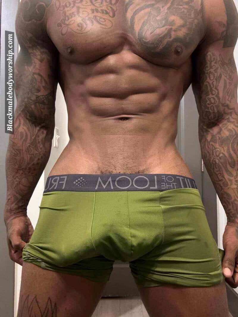 Close-up of a powerful Black male standing confidently, showing off his chiseled chest, sculpted arms, and ripped abs. He wears tight green boxer briefs, highlighting a prominent curved bulge—radiating dominance, strength, and raw sexual energy.